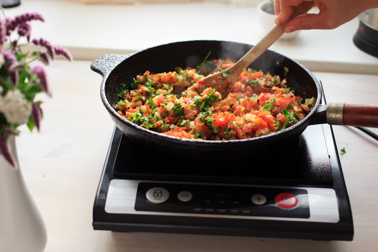 Induction cooking at home on a black portable cooker in cast iron cookware. Vegan meal with lentils, rice and vegetables