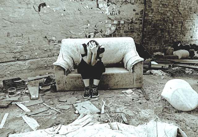 Young woman holds her head while sitting on a sofa inside a ruined house