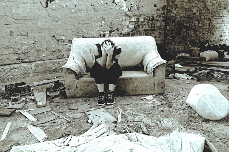 Young woman holds her head while sitting on a sofa inside a ruined house