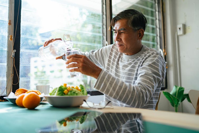 An older man pours himself a glass of water to drink with his meal.