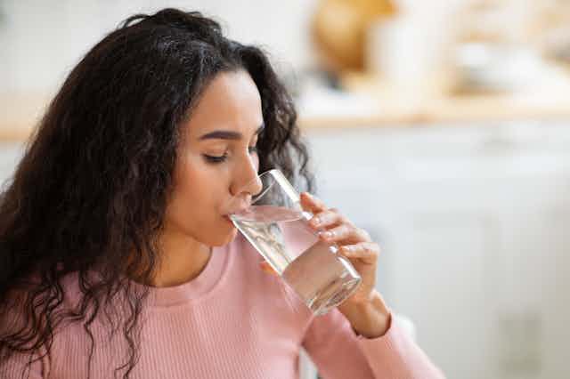 A young woman drinks a glass of water.
