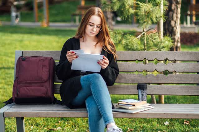 Young woman looking at paper sat on bench