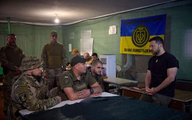 Ukraine president Volodymyr Zelensky stands in front of a natonional flag while talking with Ukrainian officers.