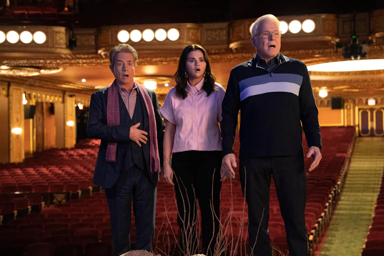 Three people stand in a theatre shocked.