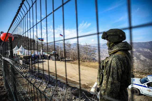 A man in fatigues stands behind a wire fence.