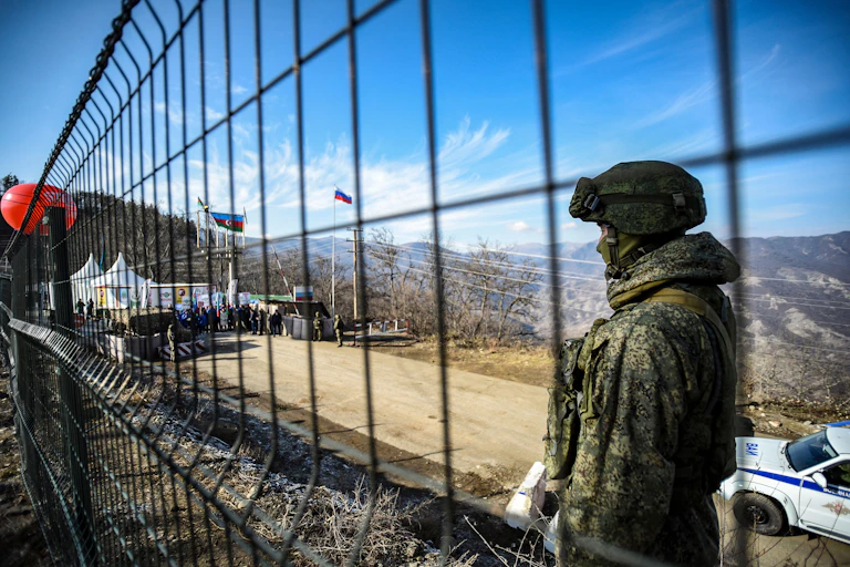 A man in fatigues stands behind a wire fence.