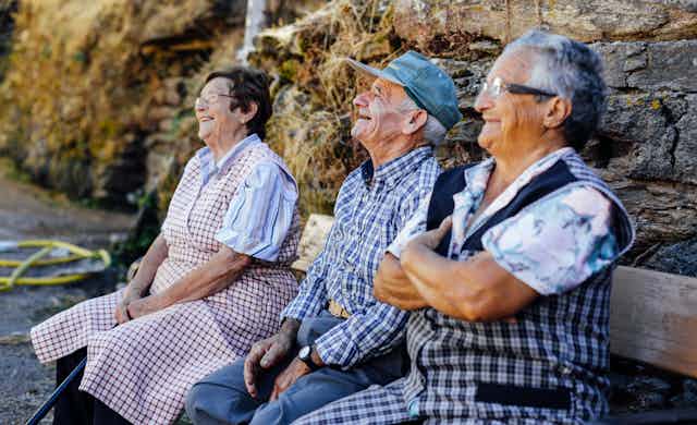 Tres ancianos sonriendo sentados en un banco.