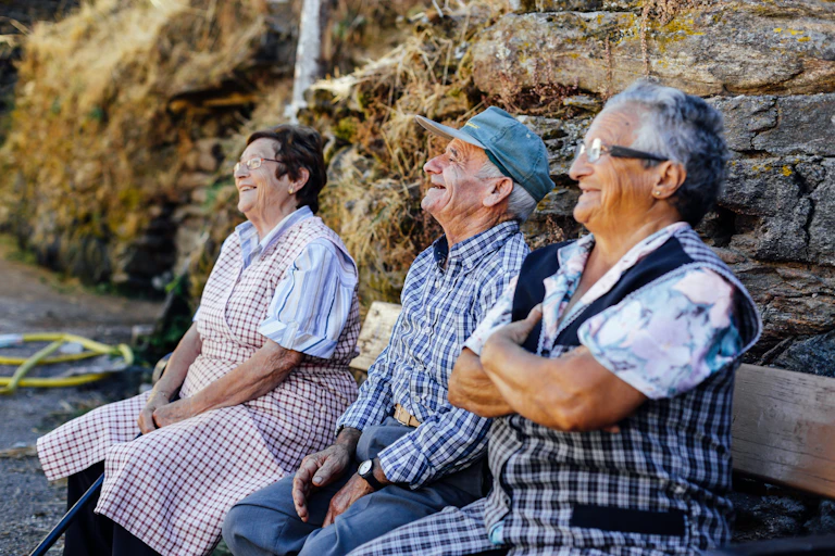 Tres ancianos sonriendo sentados en un banco.