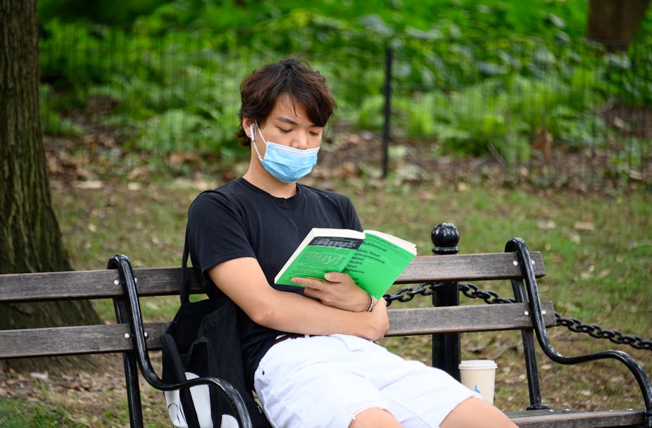 Pessoa vestindo máscara lê um livro na praça
