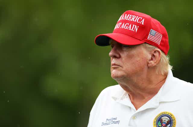A man with reddish hair and wearing a white shirt and a red hat.