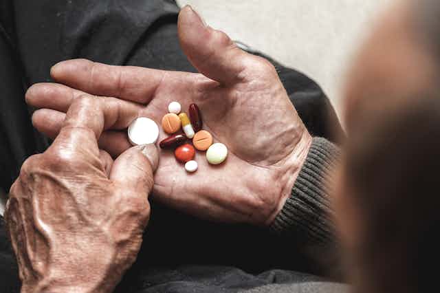 older person's hands with 10 different pills in palm