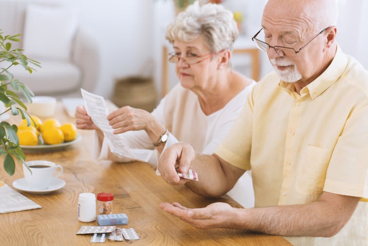 older couple sit at table looking at medications