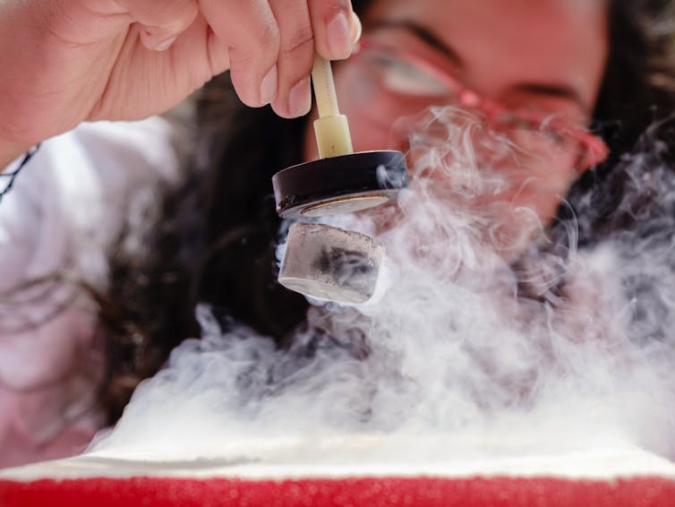 A photo shows a scientist manipulating a levitating piece of metal surrounding by vapour from liquid nitrogen.