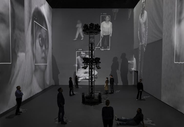 People stand under their surveilled reflections.