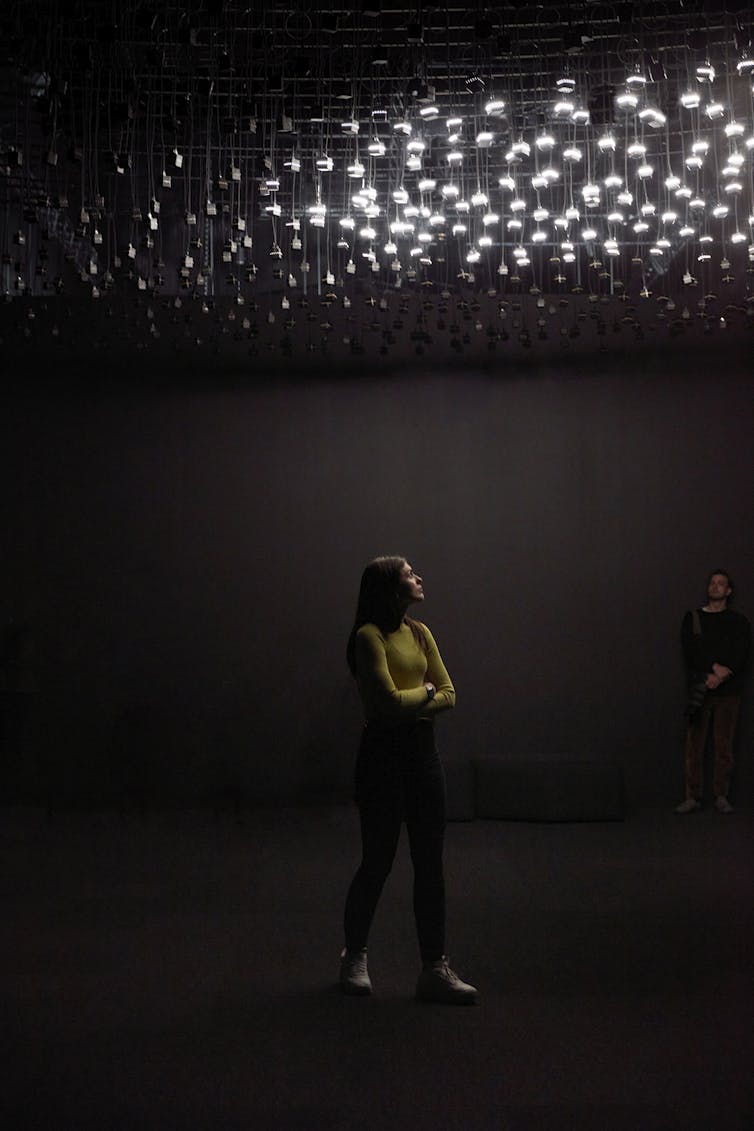 A woman stands under white lights.