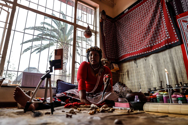 Traditional healer consulting remotely with a patient , sitting on floor