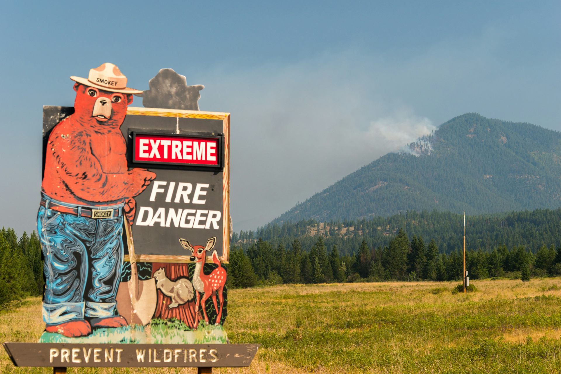 Pancarte avertissant sur le danger des feux de forets, avec derrière une montagne et de la fumée
