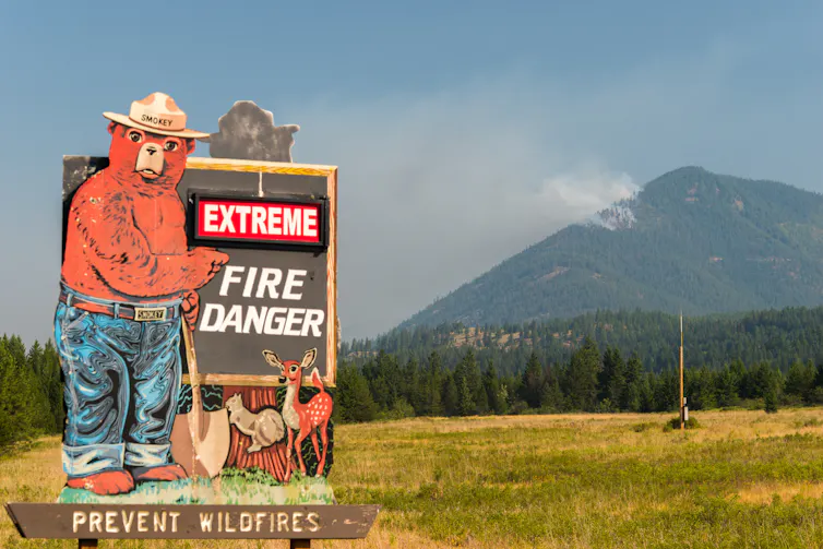 Pancarte avertissant sur le danger des feux de forets, avec derrière une montagne et de la fumée