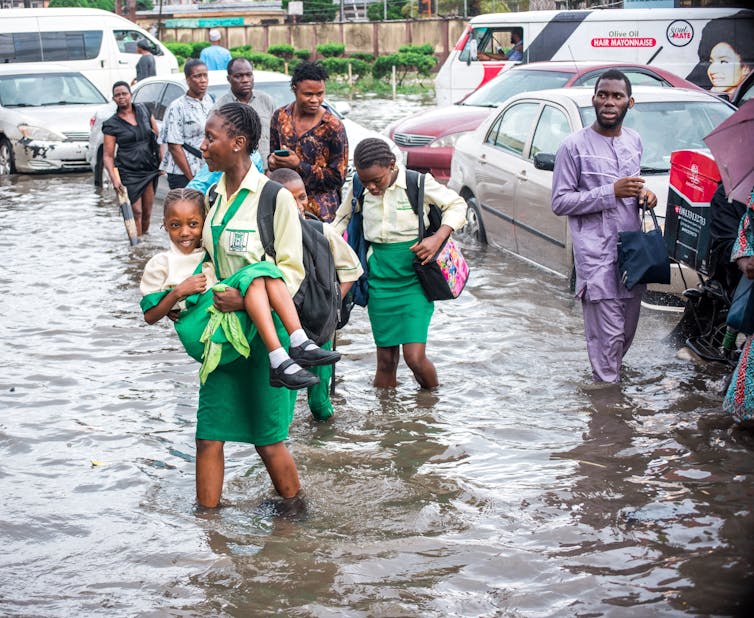 Uma jovem carregando outra garota em uma estrada inundada.