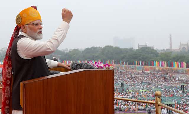 Indian PM Narendra Modi clenches his fist as he speaks from a lectern at Delhi's Red Fort on August 15 2023.