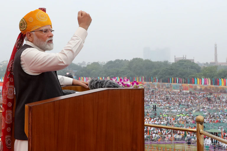 Indian PM Narendra Modi clenches his fist as he speaks from a lectern at Delhi's Red Fort on August 15 2023.