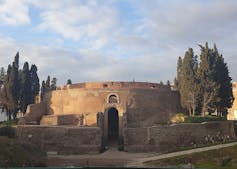 A circular walled ancient monument with cyprus trees around it.