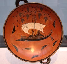 A rust colored cup with drawings of ivy, vines and dolphins.