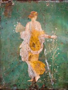 A fresco showing the back of a young woman, with head slightly turned, wearing a gown with shades of yellow.
