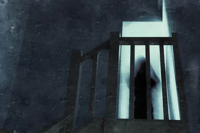 A blurry ghostly figure stands at the top of a darkened stairway.