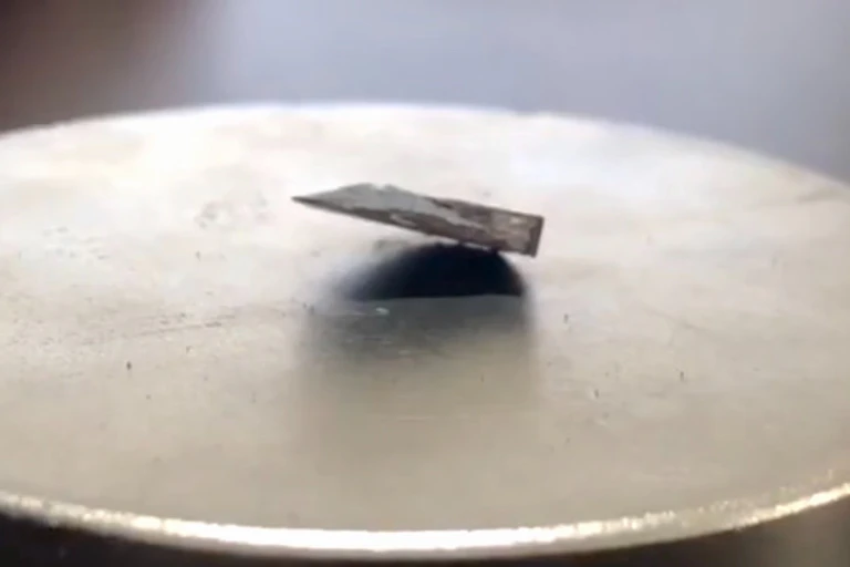 A photo showing a chip of dark material partially floating above a silver metallic magnet.