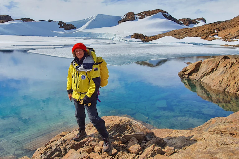 Antarctic researcher Dr Dana Bergstrom standing on the rocky shore with frozen hills in the backgrounds