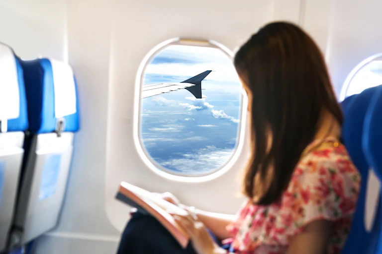 Mujer sentada en la cabina de un avión leyendo.