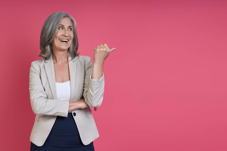A grey-haired woman flicks her thumb up against a pink background