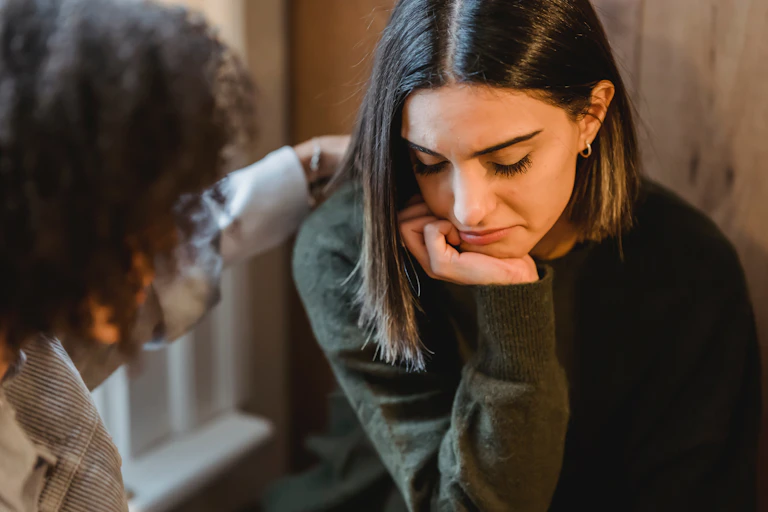 Woman looking sad is comforted by a friend.