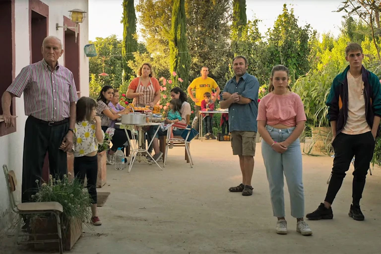 Fotograma de una película en donde se ven a diferentes miembros de una familia comiendo y mirando hacia una misma zona, situada donde la cámara.
