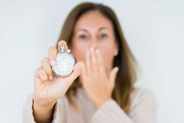 Woman holds stopwatch in one hand and covers mouth with other