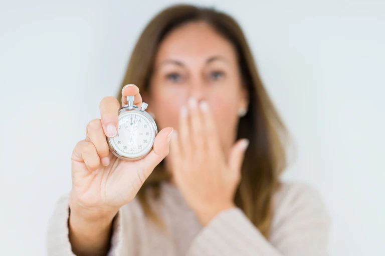 Woman holds stopwatch in one hand and covers mouth with other