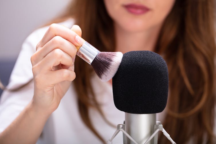 Woman brushing a microphone with a makeup brush.