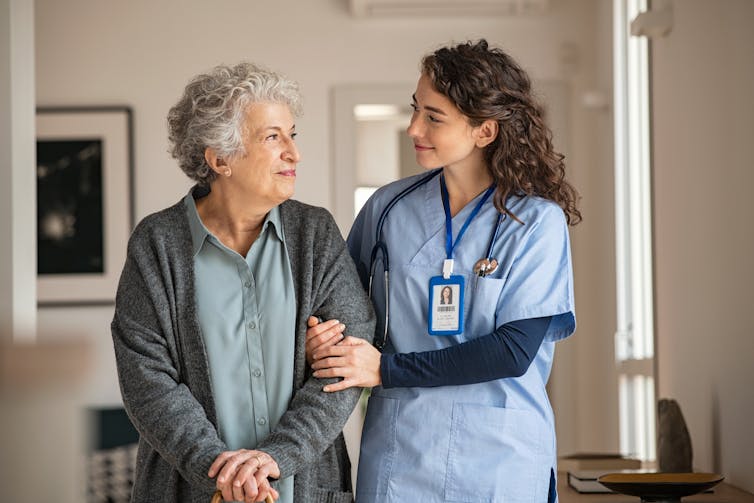 A woman with gray hair with health care worker in scrubs.