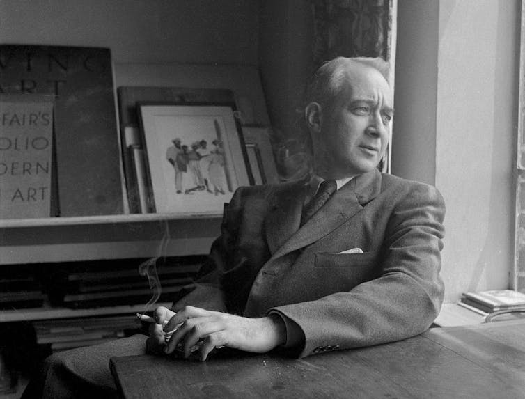 Seated man in suit holding a cigarette and looking out a window.