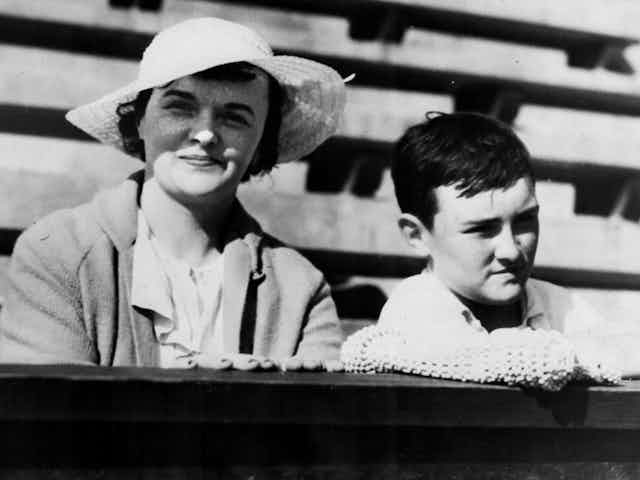 Black and white photo of woman wearing hat posing with boy in bleachers.