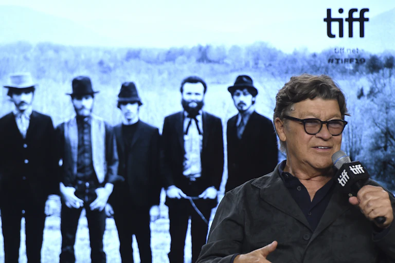 an older man in front of a tv screen showing five men standing and a TIFF logo