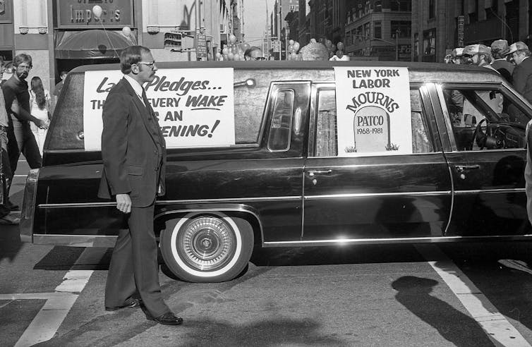 A black and white photo of a hearse with a sign that reads 'New York Labor Mourns PATCO 1968-1981.'