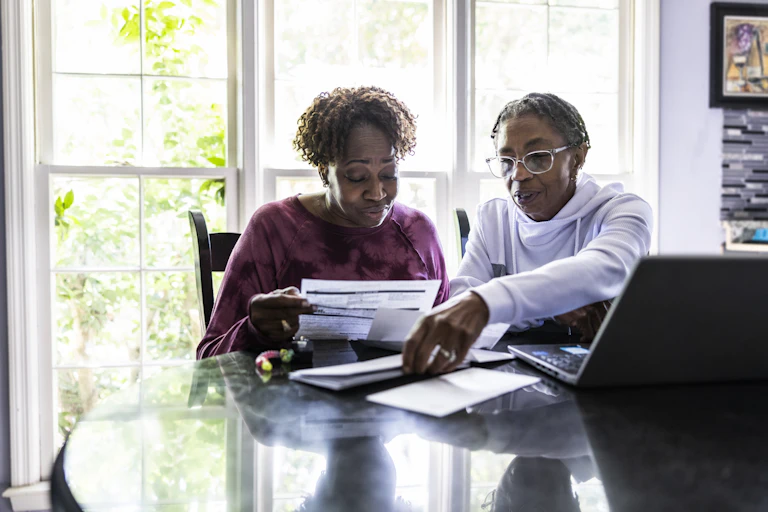 A lesbian couple pays bills at a kitchen table.