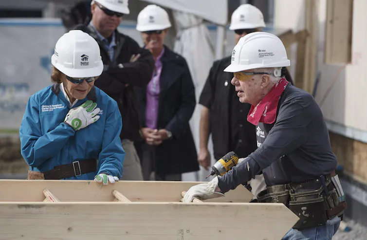 Former President Jimmy Carter and Rosalynn carter wearing white hard hats on a construction site