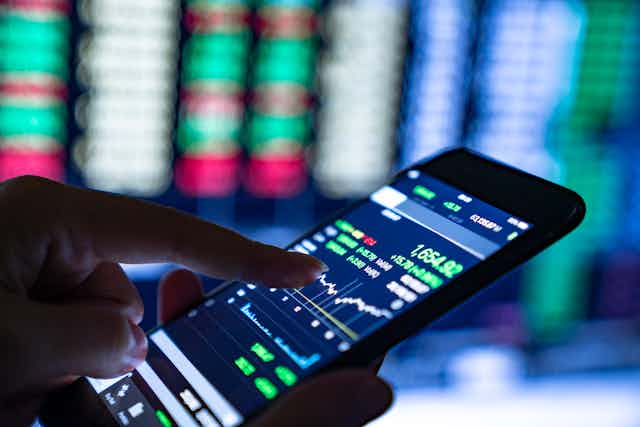 a finger touches the screen of a phone, which is displaying stock market information