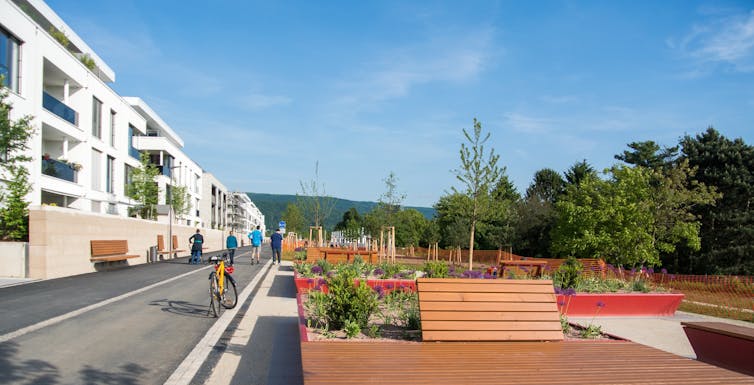 View of cycle path, benches and gardens running along the edge of white modern apartment buildings
