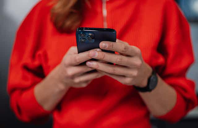 A woman in a red jumper holding a smartphone looking at messages