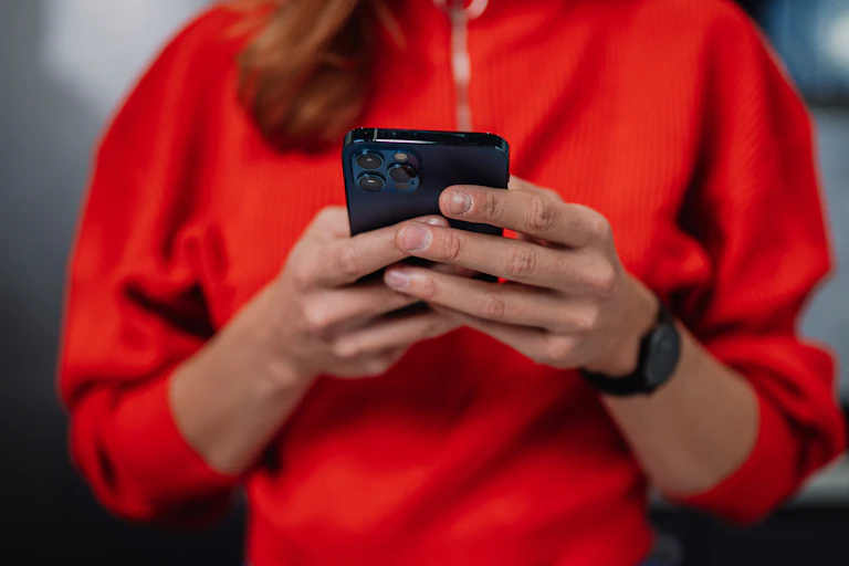 A woman in a red jumper holding a smartphone looking at messages