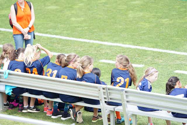 A soccer team of young girls sit on a bench